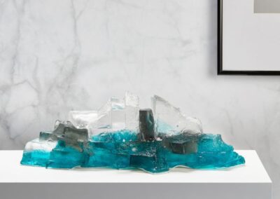 Glass sculpture on a display on a shelf. Colours aquamarine, grey and clear